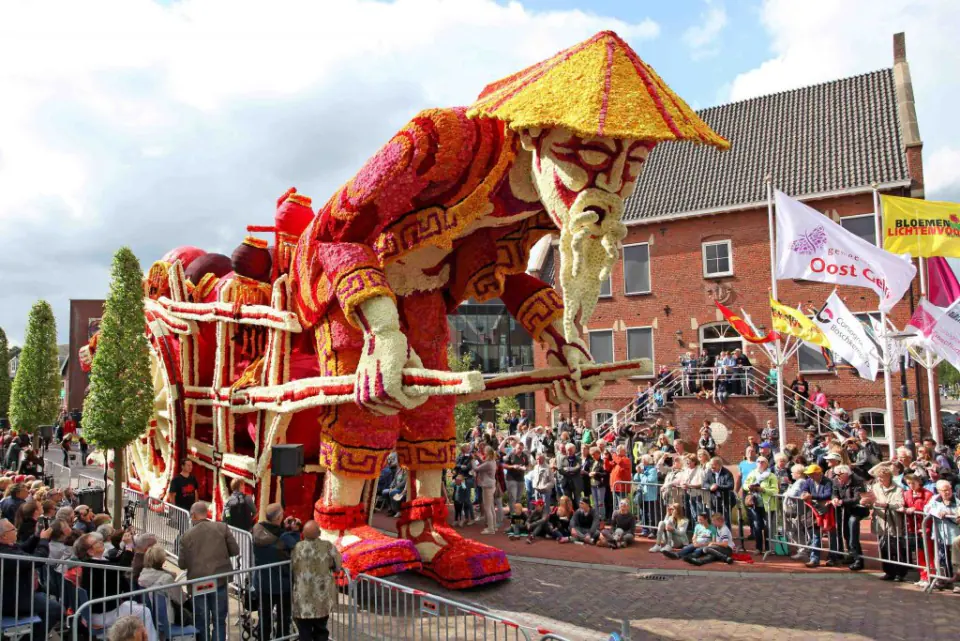 Een praalwagen van het Bloemencorso Lichtenvoorde, helemaal geplakt met rode en gele dahlia's, rijdt langs het publiek door het dorp