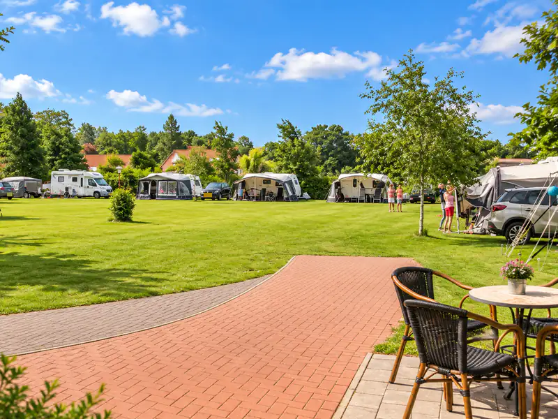 Het open kampeerveld met caravans en voortenten langs de randen, met een terras op de voorgrond