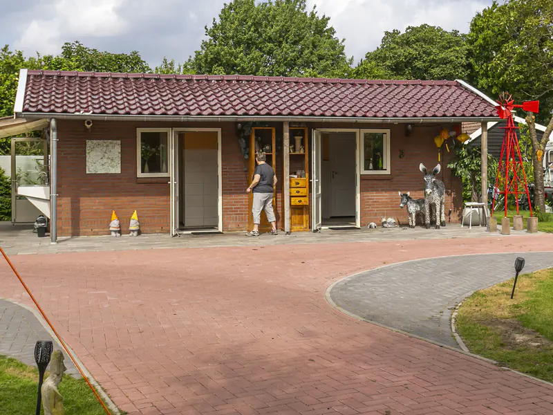 Het sanitairgebouw van buiten, met openstaande deuren onder een overdekte gang