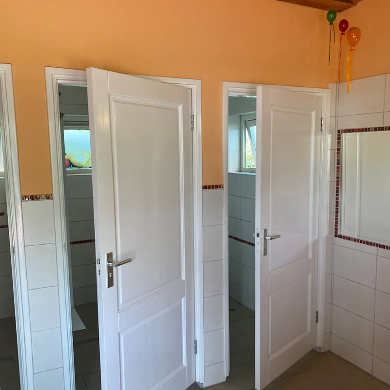 Openstaande paneeldeuren van de toiletten en doucheruimtes, met een raampje in elke ruimte