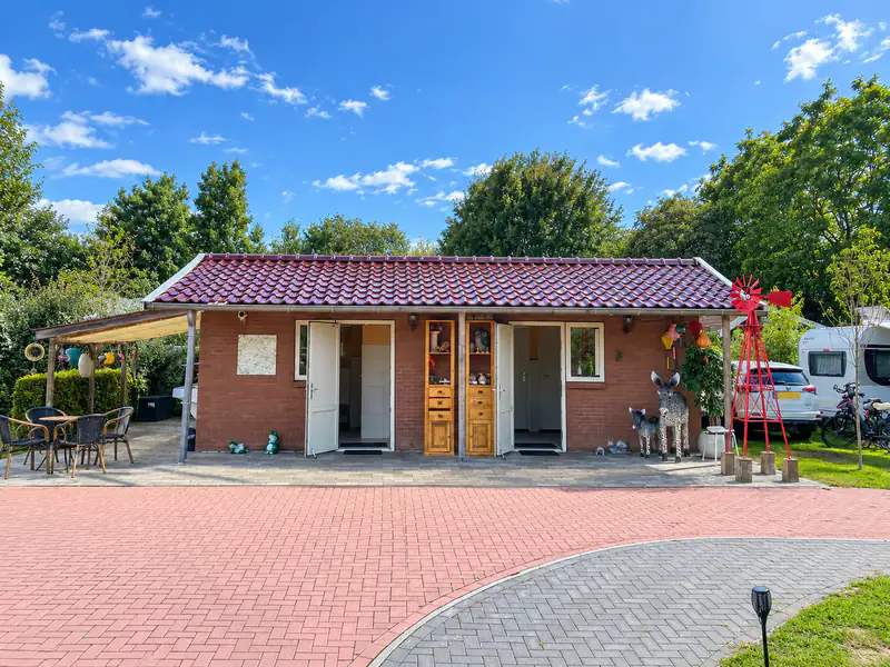 Het sanitairgebouw van buiten, met open deuren onder de overkapping en een terras met tafeltjes ernaast