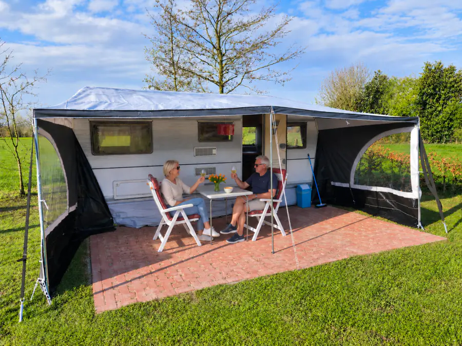 De huurcaravan met uitgeklapte luifel en twee gasten aan tafel op het terras