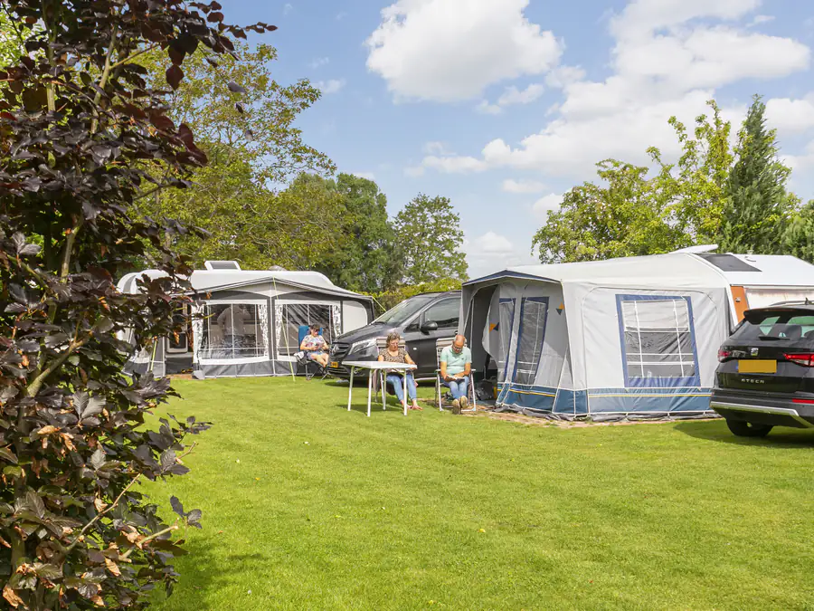 Kampeerplaatsen met caravans en voortenten, gasten aan een tafel in de zon