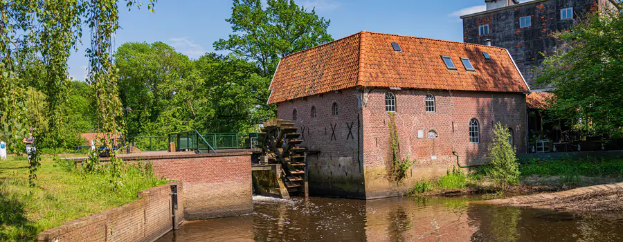 Een watermolen met rood pannendak en houten scheprad, aan het water tussen de bomen