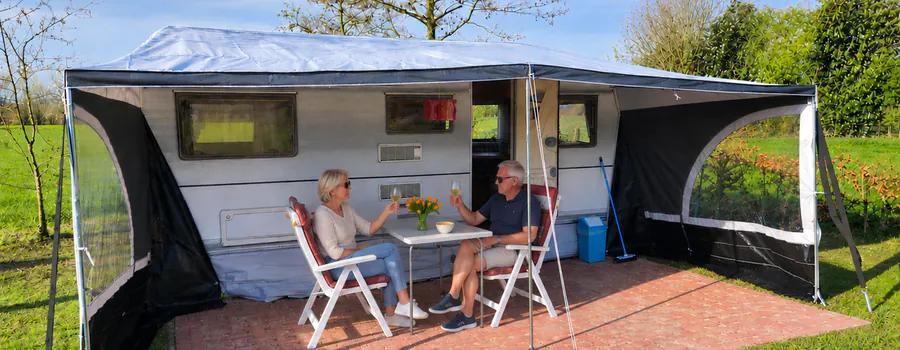 De huurcaravan met uitgeklapte luifel en twee gasten aan tafel op het terras