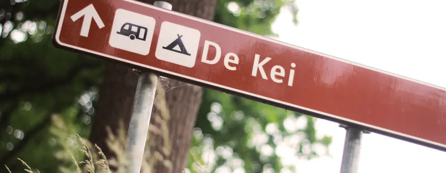 Het bruine bord langs de weg dat de weg wijst naar Camping de Kei