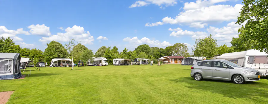 Die offene Wiese von Camping de Kei unter blauem Himmel, mit Wohnwagen und Vorzelten an den Rändern