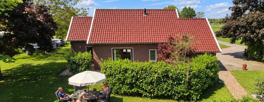 De vakantiewoning met rode dakpannen, met gasten aan tafel onder een parasol in de tuin ervoor