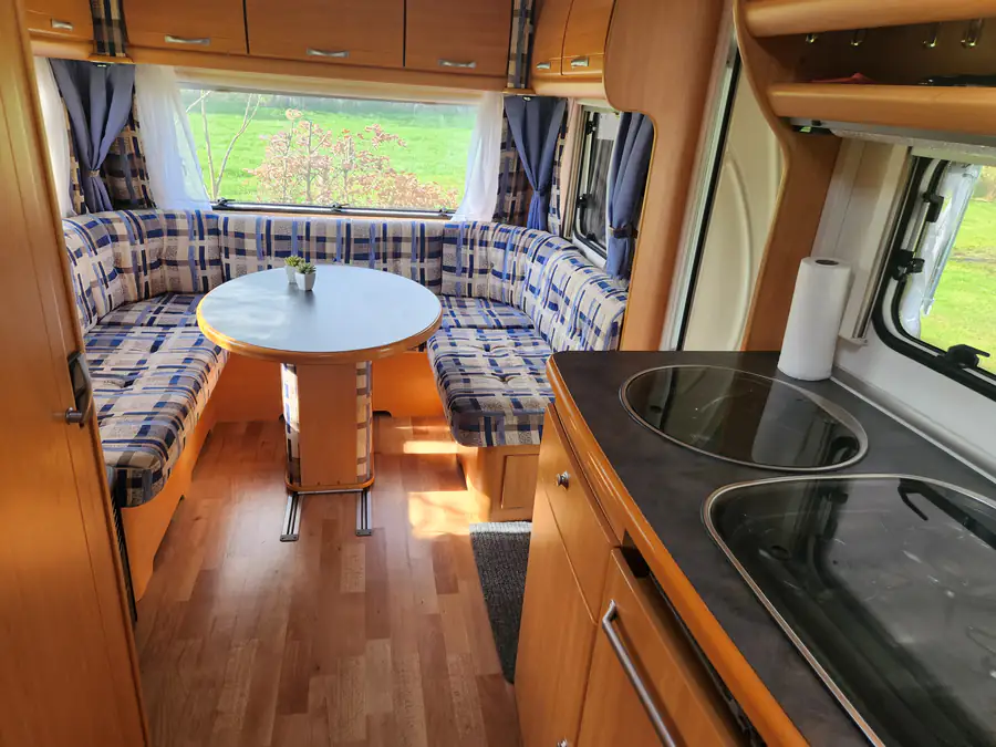 De zithoek van de huurcaravan met ronde tafel, en rechts het aanrecht met kookplaat en spoelbak