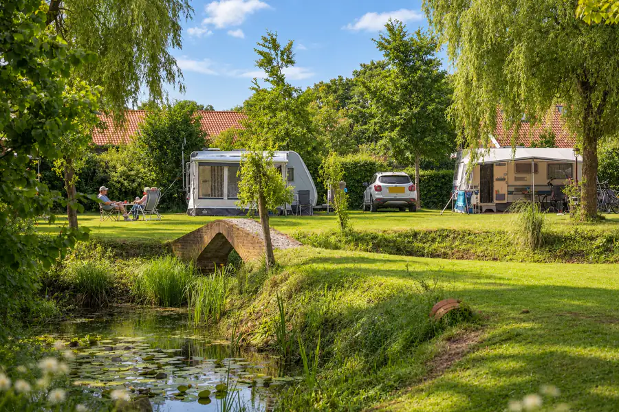 De vijver met waterlelies en het bruggetje, met daarachter caravans op het kampeerveld