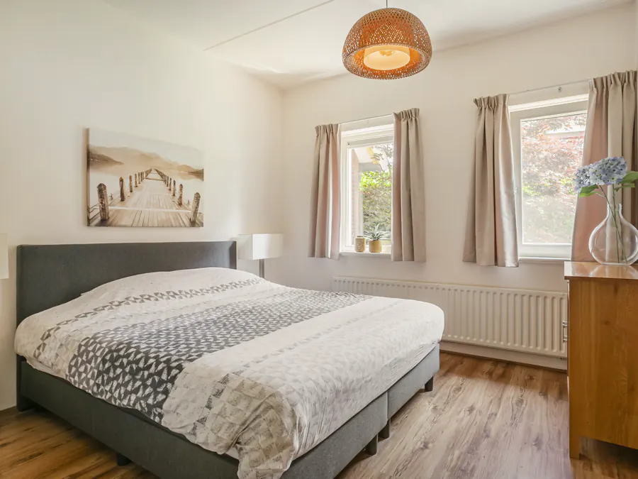 De slaapkamer beneden met kingsize bed en twee ramen op de tuin