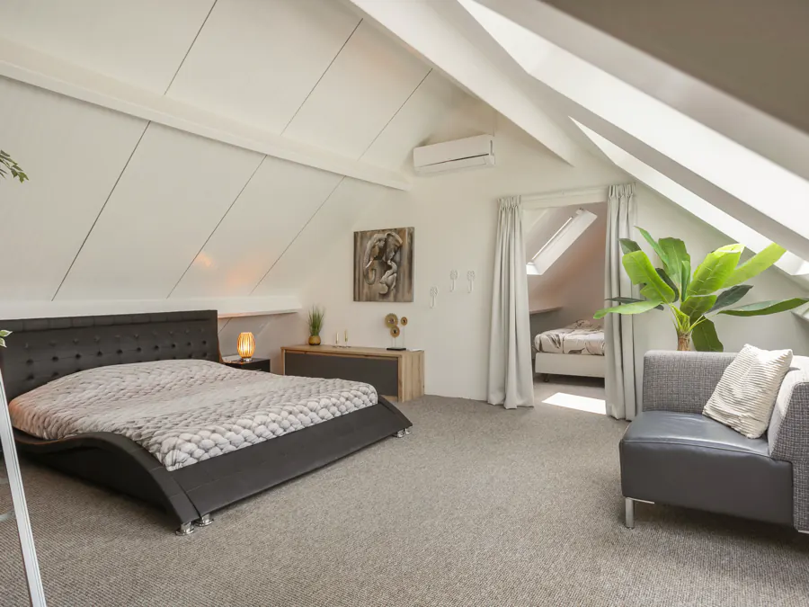 De slaapkamer boven met kingsize bed onder het schuine dak, met daarachter de derde slaapkamer