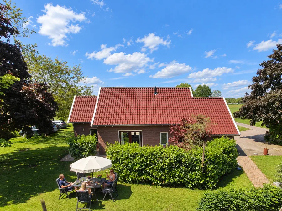 De vakantiewoning met rode dakpannen, met gasten aan tafel onder een parasol in de tuin