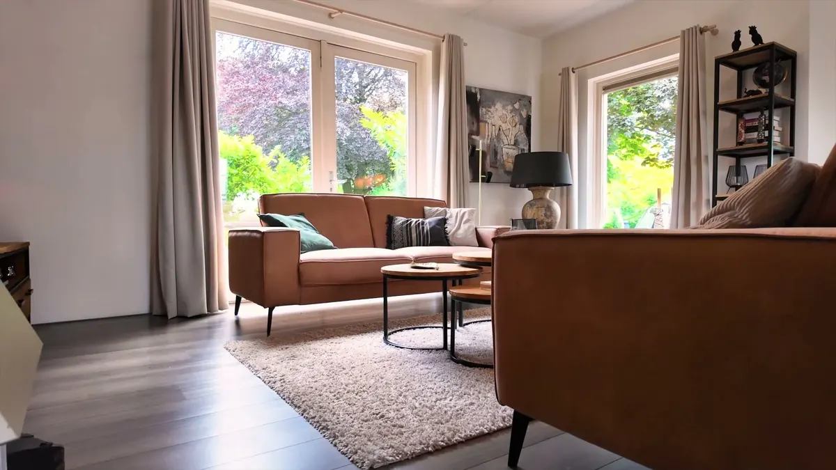 De woonkamer met bank en grote ramen op de tuin