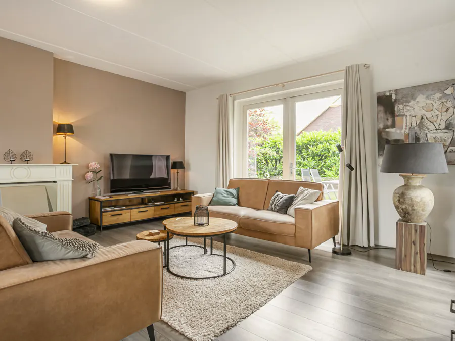 De woonkamer met twee leren banken, een televisie en openslaande deuren naar de tuin