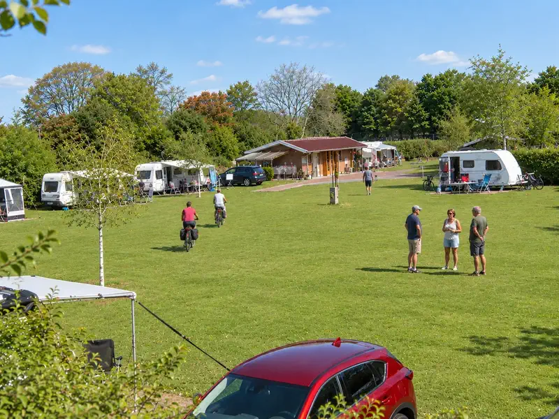Het kampeerveld met fietsers op het pad, caravans langs de randen en gasten die staan te praten