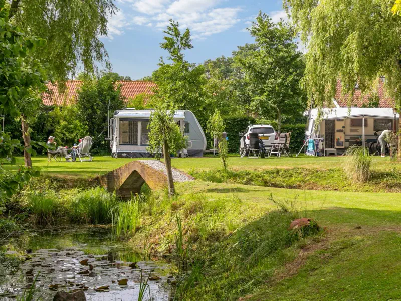 De vijver met het gemetselde bruggetje, met daarachter caravans op het kampeerveld