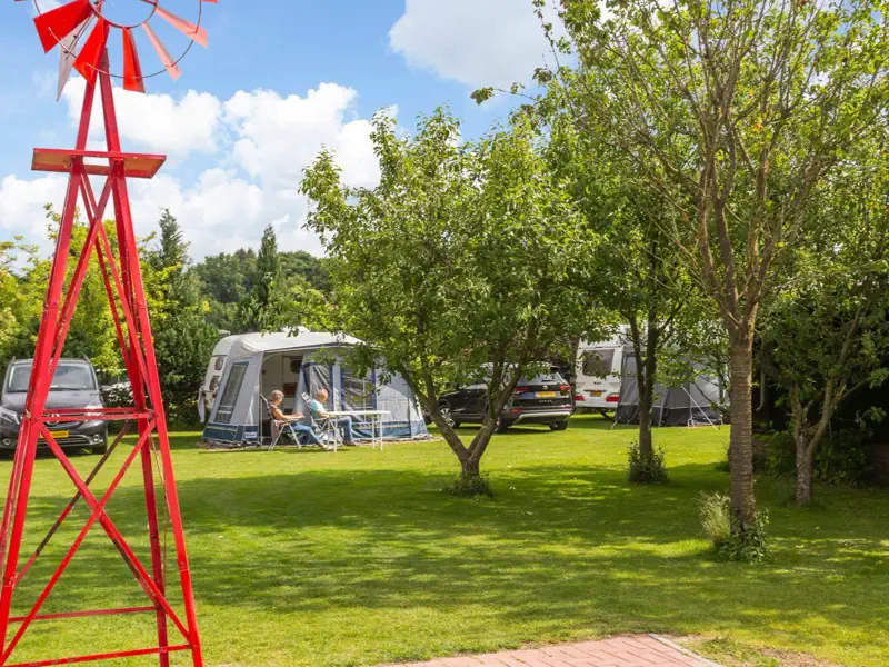 De rode windmolen op het veld, met daarachter een caravan en gasten aan tafel